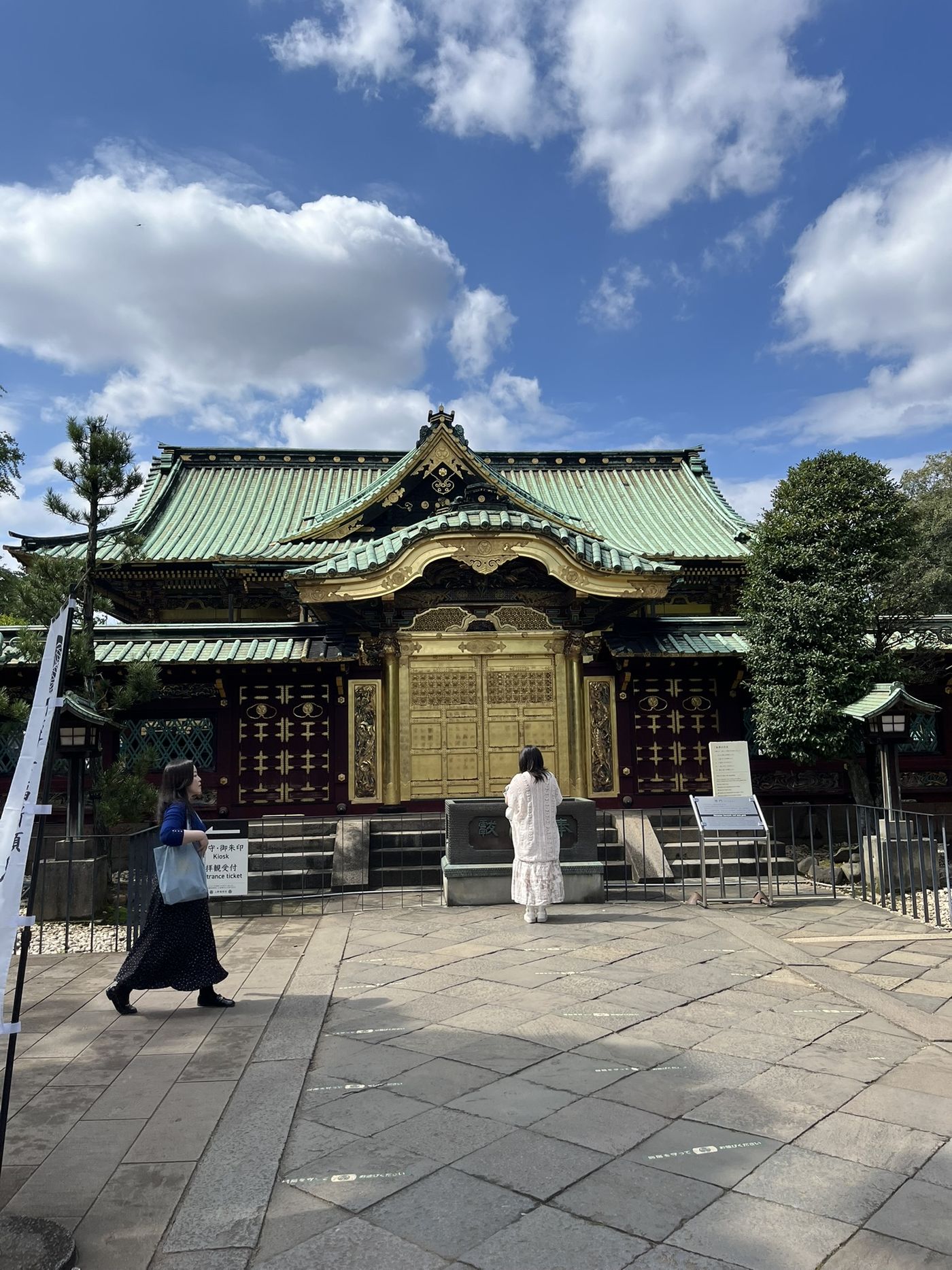 Een Japanse tempel met een groen dak en gouden deuren onder een blauwe lucht, met een vrouw die voor de ingang staat